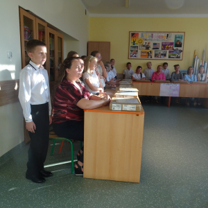 Duża grupa rodziców i uczniów klasy czwartej zgromadzonych w sali szkolnej, podczas przekazania laptopów uczniom. Uczniowie w strojach galowych. Kliknięcie na zdjęcie spowoduje jego powiększenie do oryginalnego rozmiaru.