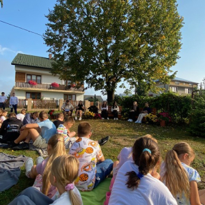 Uczniowie siedzą wokół lipy podczas narodowego czytania.  Kliknięcie w zdjęcie spowoduje powiększenie do oryginalnego rozmiaru.