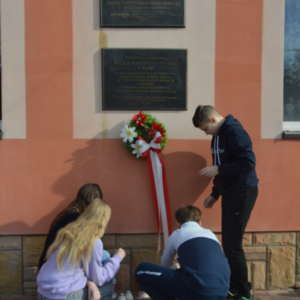 Uczniowie zapalają znicze przed pamiątkową tablicą. Kliknięcie na zdjęcie spowoduje jego powiększenie do oryginalnego rozmiaru.