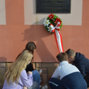Uczniowie zapalają znicze przed pamiątkową tablicą. Kliknięcie na zdjęcie spowoduje jego powiększenie do oryginalnego rozmiaru.